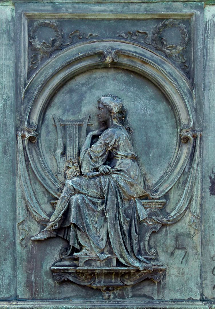 Monument of Beethoven (Bonn) Sockelrelief, links unterhalb von Beethoven; Frauengestalt mit Lyra-Harfe, einer griechischen Maske auf ihrem Schoß und einer Maske auf dem Kopf